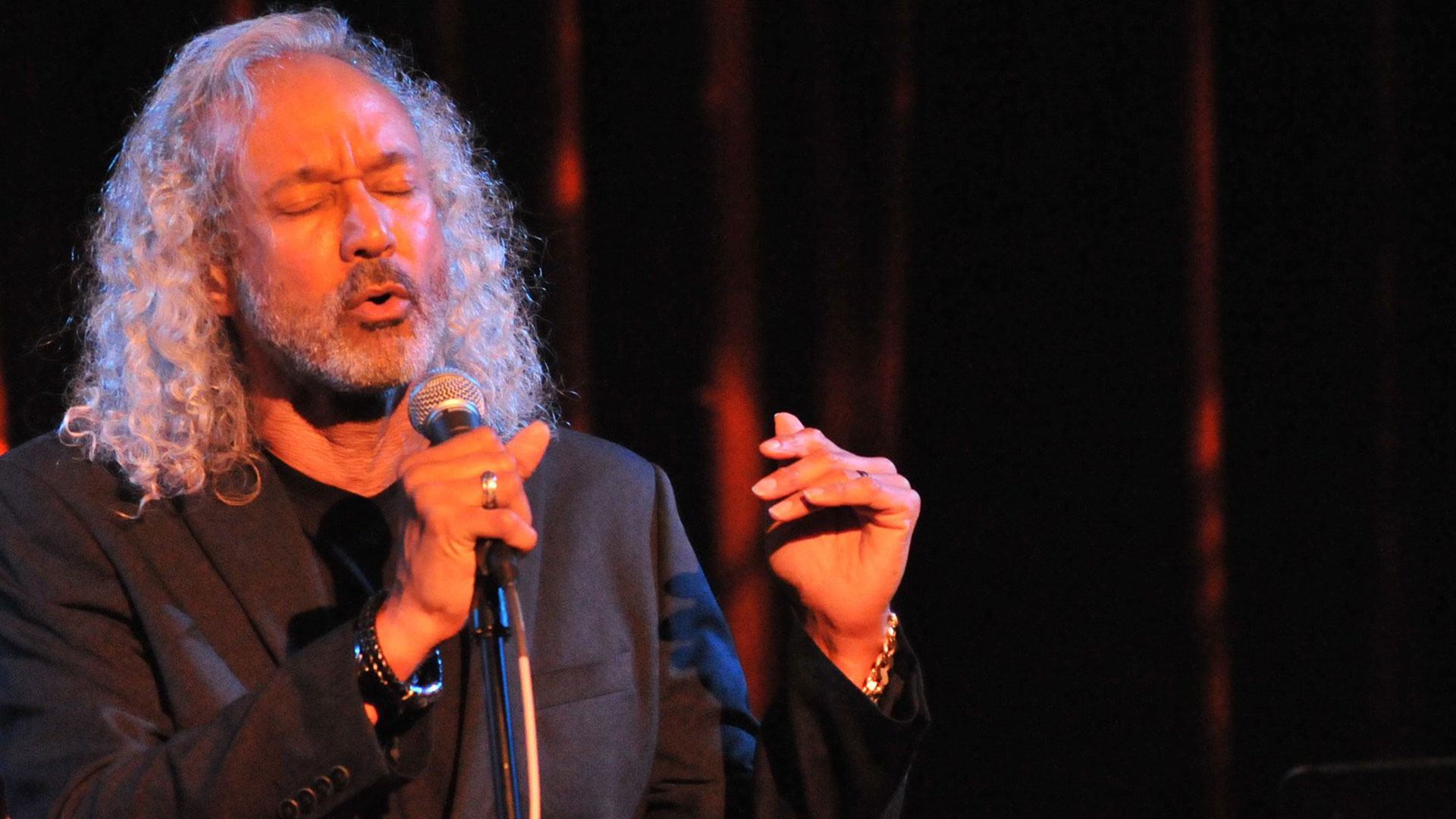 A man with curly hair and beard holding a microphone.